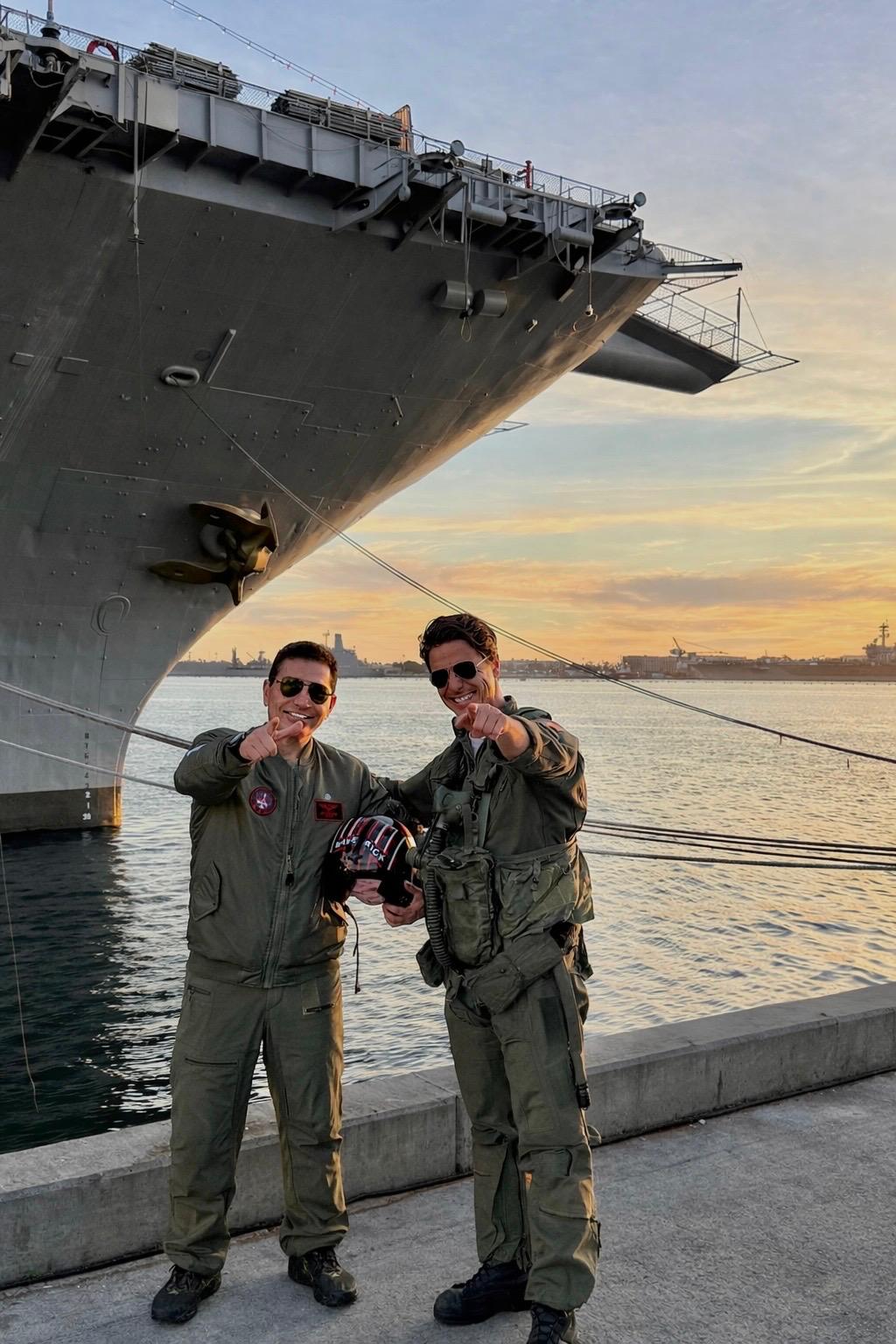 Fred Khalilian and Tom Cruise in flight suits pointing at camera at USS carrier